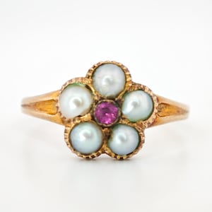 May include: A gold ring with a floral design. Five white pearls form the petals, encircling a small, round, pink gemstone at the centre. The ring has a plain band. The ring is a classic piece of jewellery.