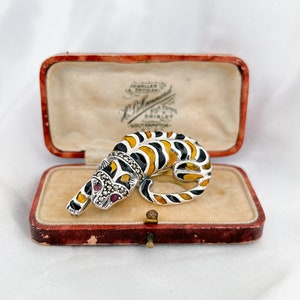 May include: A silver and black enamel tiger brooch with red ruby eyes, set in a red velvet lined box with the inscription "Jeweller & Optician H.O. Armand High Street Shirley Southampton".