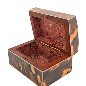 May include: An open, rectangular wooden box with a hinged lid. The exterior features a tortoiseshell pattern in shades of brown and amber. The interior is lined with a red and gold marbled design. The box is empty.