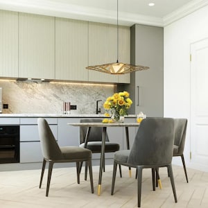 Op de afbeelding: Een moderne eetkamer met een lichte houten vloer, een witte keuken met grijze kasten, een zwarte oven en een tafel met vier grijze stoelen. Een geometrische lamp hangt boven de tafel. Een boeket gele bloemen staat op de tafel.