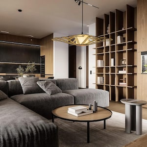 Op de afbeelding: Een moderne woonkamer met een grote hoekbank in een donkergrijze stof. De bank staat voor een groot raam met natuurlijk licht. Een houten salontafel met een geometrisch ontwerp staat voor de bank. Een grote, geometrische lamp hangt aan het plafond. De kamer heeft een minimalistisch ontwerp met een focus op natuurlijke materialen.