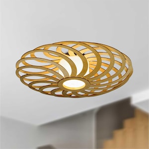 May include: An oval wooden ceiling light. The light fitting features a spiral design made of curved wooden strips. The central light source emits a warm glow. The fixture is mounted on a white ceiling. The light's dimensions are approximately 60 cm in diameter.