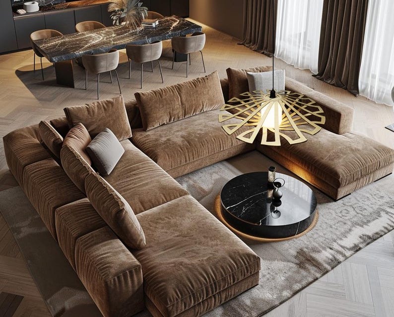 Op de afbeelding: Een grote bruine hoekbank met een zwarte marmeren salontafel en een gouden geometrische hanglamp erboven. De bank is in een L-vorm geplaatst en heeft verschillende kussens en kussens.