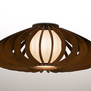 May include: A brown wooden ceiling light fixture with a white fabric shade. The light fixture has a unique design with multiple layers of wood that create a fan-like shape.