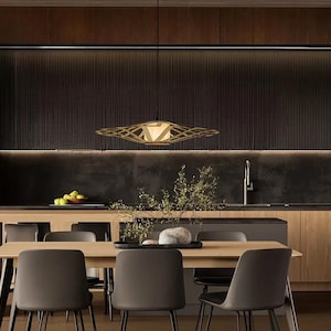 Op de afbeelding: Een moderne eetkamer met een houten tafel en stoelen. De tafel is gedekt met een vaas met bloemen en een kom met fruit. Een grote, geometrische lamp hangt boven de tafel.