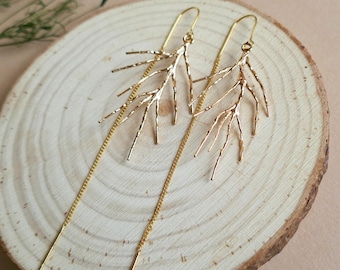 May include: A pair of gold-toned threader earrings featuring a textured, branch-like design. Each earring consists of a delicate metal chain that transitions into a rigid, twig-shaped element with multiple thin, pointed extensions radiating outwards.