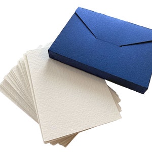 May include: A stack of white paper cards with a blue envelope. The envelope has a flap and is made of textured paper.