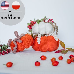 May include: Three crocheted pumpkins in orange and white, decorated with greenery and berries. The pumpkins are stacked, with one orange pumpkin on the bottom, a white pumpkin in the middle, and another orange pumpkin on top. The text "PDF CROCHET PATTERN" is visible.
