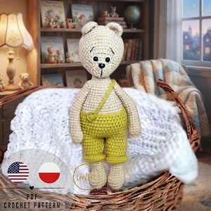 Puede incluir: Un oso de ganchillo de color crema con ojos y nariz negros, que lleva pantalones cortos de ganchillo de color amarillo brillante con una correa a juego. El oso está colocado en una cesta de mimbre. La imagen incluye el texto PDF CROCHET PATTERN.