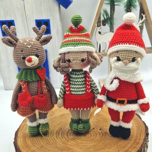 May include: Three handmade crochet Christmas figures: a reindeer, an elf, and Santa Claus. The reindeer is brown with antlers, a red nose, and a green scarf. The elf wears a green and red outfit. Santa Claus is in a red suit with a white beard and hat.