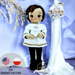 May include: Crochet pattern for a white crocheted doll wearing a white dress with gold trim and the letters "IHS" on the front. The doll has brown hair and brown eyes. The doll is standing on a white surface.