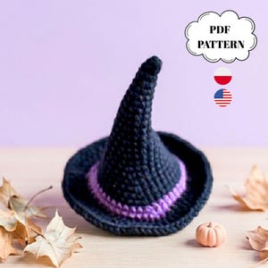 May include: A black crochet witch hat with a purple band around the brim. The hat is cone-shaped with a wide brim. The text "PDF PATTERN" is in a white cloud-shaped graphic. A small pumpkin and fall leaves are in the background.
