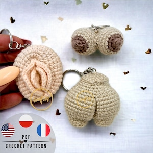 May include: Three crocheted keychains in the shape of body parts. The keychains are beige and brown. The keychains are on a white background with small hearts scattered around them. The text "PDF CROCHET PATTERN" is at the bottom of the image.