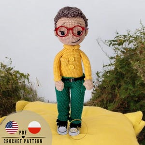 May include: A handmade crochet doll of a person wearing red glasses, a yellow sweater, green pants, and black shoes. The doll has brown hair and a neutral skin tone. The doll is standing on a yellow surface. The image includes the text "PDF CROCHET PATTERN".