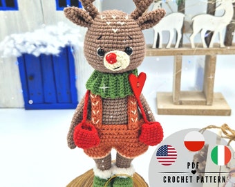 May include: A crocheted reindeer doll with brown antlers, a red nose, and a green scarf. The reindeer wears orange dungarees and red mittens. The doll is standing on a wooden slice. The image includes the text "PDF CROCHET PATTERN".