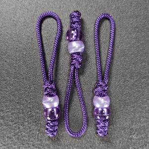 May include: Three purple beaded lanyards with a loop at the top. Each lanyard features a series of purple beads and a decorative knot. The beads are a mix of clear and opaque purple.