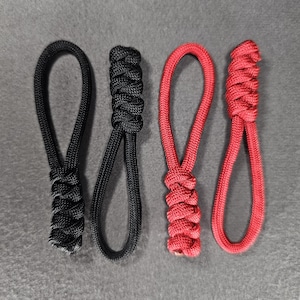 May include: Four zipper pulls, two black and two red, arranged in a row. Each pull features a loop and a braided knot at the base. The pulls are made of a durable, woven material.