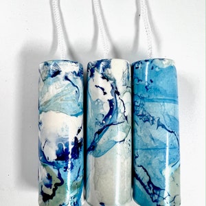 May include: Three cylindrical ceramic pull chains with white cords. The cylinders have a marbled design in shades of blue, white, and a touch of green. The pull chains are hanging against a white background.