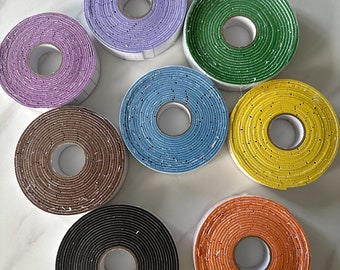 May include: Eight rolls of colorful tape with a textured surface. The rolls are arranged in a circle on a white marble surface.