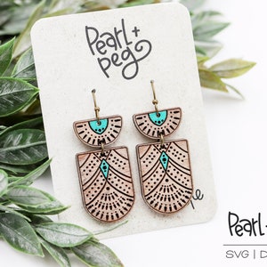 Puede incluir: Un par de pendientes de madera con un diseño geométrico en marrón y turquesa. Los pendientes cuelgan de una tarjeta blanca con el texto "Pearl + Peg" escrito en negro.
