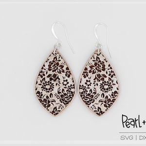 May include: A pair of dangle earrings with a white background and a brown floral pattern. The earrings are made of wood and have silver hooks.