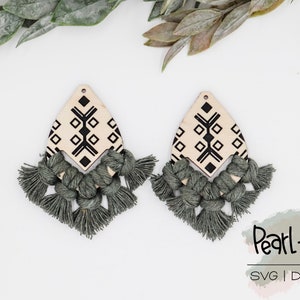 May include: A pair of wooden earrings with a geometric pattern and green tassels. The earrings are on a white background with green leaves.