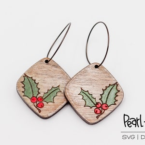 May include: A pair of wooden earrings with a holly design. The earrings are painted in a light brown color with green holly leaves and red berries. The earrings are attached to silver hoops.