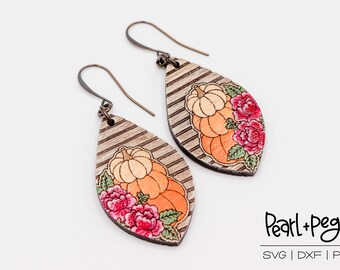 Puede incluir: Un par de pendientes de madera con forma de lágrima. Los pendientes tienen un patrón de veta de madera y un diseño de calabazas y flores en tonos naranja, rojo y verde. Los pendientes cuelgan de ganchos plateados.
