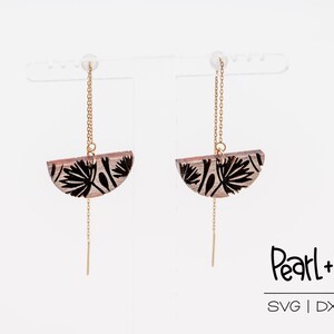 May include: A pair of dangle earrings with a gold chain and a half-circle wooden pendant featuring a black floral design. The earrings are displayed on a white stand. The text "Pearl+Peg SVG | DXF | PDF" is visible below the earrings.