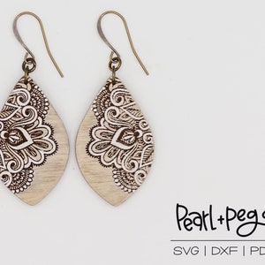 May include: A pair of wooden earrings with a white and brown intricate design. The earrings are shaped like teardrops and have a gold hook.