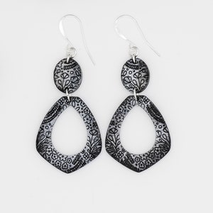 Puede incluir: Un par de pendientes de plata con dise&ntilde;os florales en blanco y negro. Los pendientes est&aacute;n hechos de dos piezas, una pieza ovalada m&aacute;s peque&ntilde;a y una pieza m&aacute;s grande en forma de l&aacute;grima.