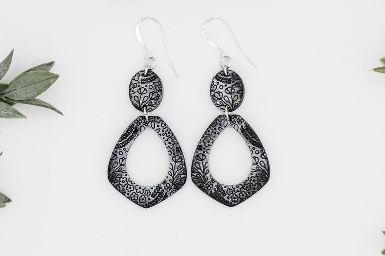 Puede incluir: Un par de pendientes de plata con dise&ntilde;os florales en blanco y negro. Los pendientes est&aacute;n hechos de dos piezas, una pieza ovalada m&aacute;s peque&ntilde;a y una pieza m&aacute;s grande en forma de l&aacute;grima.