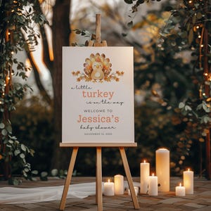 Puede incluir: Un caballete de madera exhibe un letrero de bienvenida para un baby shower. El letrero presenta una ilustraci&oacute;n de un pavo de dibujos animados y el texto "a little turkey is on the way". El letrero da la bienvenida al baby shower de Jessica, el 15 de noviembre de 2025.
