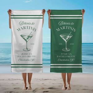May include: Two white beach towels with green stripes. The towels feature a martini glass with olives and the text "Bikinis & Martinis" with the year 2025. The text "Jessica's Bachelorette Charleston, SC" is also on the towels.