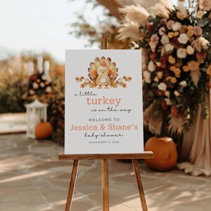 Puede incluir: Un caballete de madera exhibe un letrero con una ilustraci&oacute;n de pavo y el texto "a little turkey is on the way". Da la bienvenida a los invitados al baby shower de Jessica & Shane el 15 de noviembre de 2025. El letrero est&aacute; decorado con colores oto&ntilde;ales.