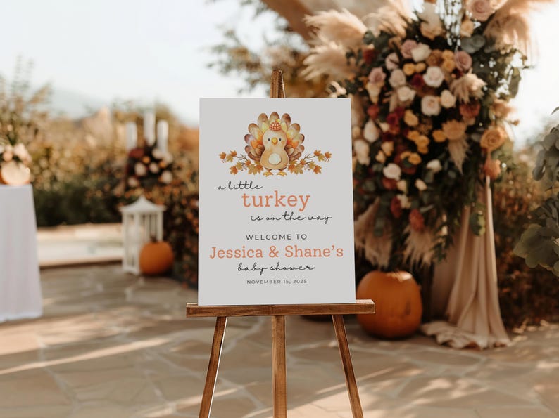 Puede incluir: Un caballete de madera exhibe un letrero con una ilustraci&oacute;n de pavo y el texto "a little turkey is on the way". Da la bienvenida a los invitados al baby shower de Jessica & Shane el 15 de noviembre de 2025. El letrero est&aacute; decorado con colores oto&ntilde;ales.