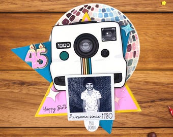 May include: A birthday card with a white camera design, a photo, and the number 45. The photo says "Awesome since 1980". The card is on a wooden surface with colorful confetti and ribbon.
