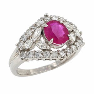 Puede incluir: Un anillo de tono plateado con un rubí central de corte ovalado en un vibrante color rojo rosado. El rubí está rodeado por un halo de pequeños diamantes de corte redondo y corte marquesa engastados en un marco de metal sobre una banda pulida.