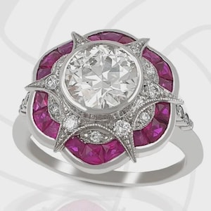 Puede incluir: Un anillo plateado con un gran diamante redondo y transparente en el centro, rodeado de diamantes más pequeños y gemas rosas vibrantes. El anillo presenta un diseño intrincado de inspiración Art Déco con una banda detallada.