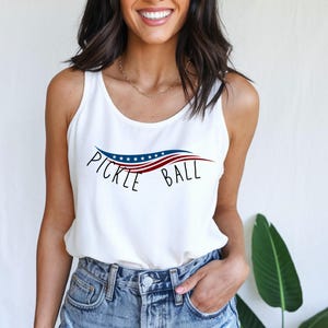 May include: White tank top with a red, white, and blue American flag design and the text "Pickle Ball" in black.