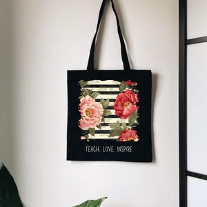 Puede incluir: Una taza de cer&aacute;mica blanca con asa negra y el texto "But First, Coffee" en negrita negra. La taza se encuentra sobre un fondo borroso, sugiriendo un ambiente acogedor.