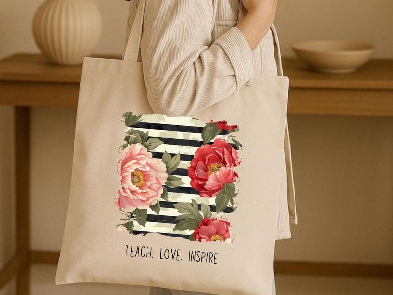 Puede incluir: Bolso tote beige con un dise&ntilde;o floral de peon&iacute;as rosas y rojas, hojas verdes y rayas blancas y negras. El texto "TEACH. LOVE. INSPIRE" est&aacute; impreso en la parte inferior. Un accesorio elegante y pr&aacute;ctico.