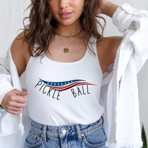 May include: White tank top with a red, white, and blue American flag design and the text "Pickle Ball".