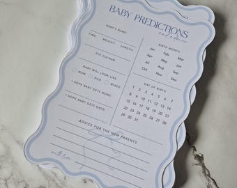 May include: A stack of baby prediction cards with a light blue scalloped edge. The cards have spaces for baby's name, time, weight, length, eye color, and birth details. Text includes "Baby Predictions and Advice."