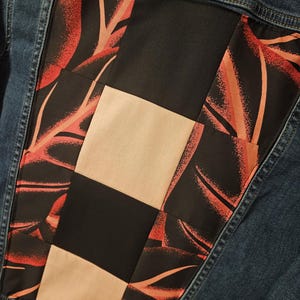 Puede incluir: Una chaqueta de mezclilla azul oscuro con un panel trasero rectangular hecho de un dise&ntilde;o de patchwork. El panel consta de cuadrados negros s&oacute;lidos, cuadrados beige s&oacute;lidos y tela negra con un patr&oacute;n de hojas rojas y naranjas.