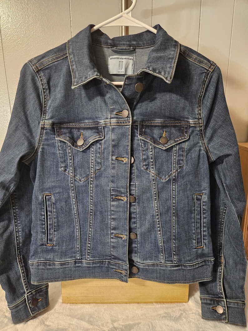 Puede incluir: Una chaqueta de mezclilla azul de lavado medio con cuello cl&aacute;sico, mangas largas con pu&ntilde;os abotonados y cierre frontal de botones. La chaqueta incluye dos bolsillos en el pecho con solapas abotonadas, dos bolsillos laterales y una etiqueta Amazon Essentials.