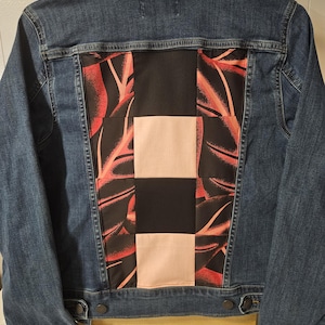 May include: A blue denim jacket featuring a back panel with a patchwork design. The panel consists of alternating squares of solid black fabric, solid light pink fabric, and black fabric with a red leaf pattern, stitched into the denim back.
