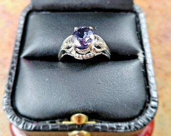 May include: A silver ring with a purple gemstone in a black ring box.