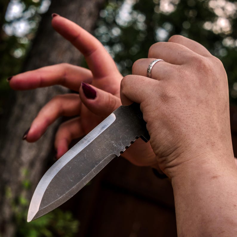 May include: A fixed-blade knife with a dark, matte-finished steel blade and a sharp, polished edge. The spine of the blade features a series of small, semi-circular notches near the handle, providing a textured grip for the thumb or fingers.
