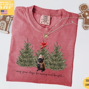 Könnte beinhalten: Karmesinrotes T-Shirt mit weihnachtlichem Design. Es zeigt drei geschmückte Weihnachtsbäume und eine Mops mit Hut und Schal. Der Text "may your days be merry and bright" steht darunter. Marke Comfort Colors.
